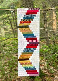 a multicolored quilt hanging from a tree in the woods with trees behind it