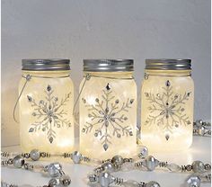 three mason jars with snowflakes on them sitting next to silver bells and beads