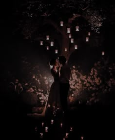 a man and woman standing under a tree in the dark with lanterns hanging from it