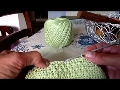 someone is crocheting a green ball on a table with other items in the background