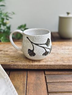 a white coffee cup sitting on top of a wooden table next to a potted plant