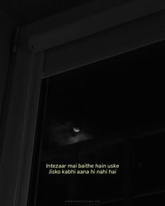 a black and white photo of a cat looking out a window at the night sky