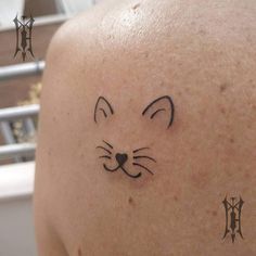 a cat tattoo on the back of a man's shoulder and neck, with two symbols above it