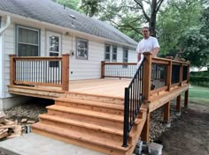 a man standing on top of a wooden deck next to a white house and trees