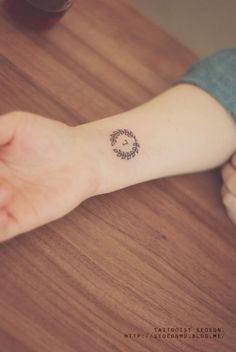 a person's arm with a small tattoo on the wrist that has a circular design