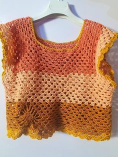 an orange and yellow crocheted top hanging on a hanger