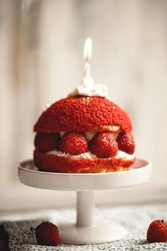 a cake with strawberries on it and a lit candle in the middle is sitting on a plate