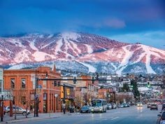 the mountains are covered in snow as cars drive down the street near buildings and traffic lights