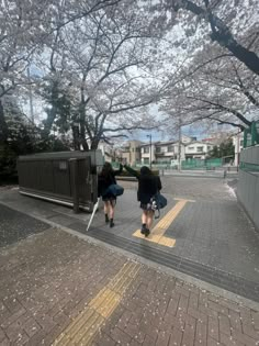 two people are walking down the sidewalk under cherry blossoms