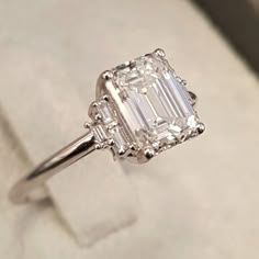 an emerald cut diamond ring sits on top of a box