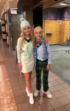 two people standing next to each other in front of a train station entrance wearing matching outfits