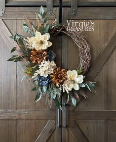 a wreath with flowers and leaves hanging on the front door to decorate it's entrance