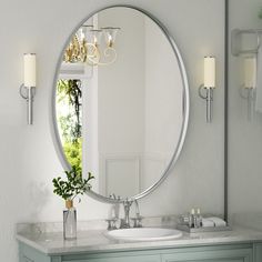 a bathroom with a large round mirror above the sink and two candles on the wall