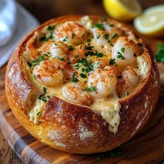 a bread bowl filled with shrimp and cheese on top of a wooden cutting board next to lemon wedges