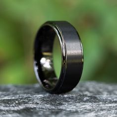 a black wedding ring sitting on top of a rock