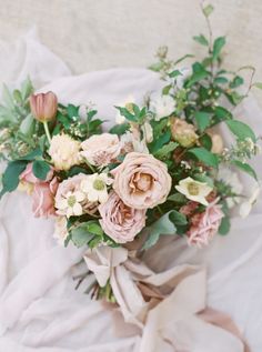 a bouquet of flowers on top of a white sheet with green leaves and pink blooms