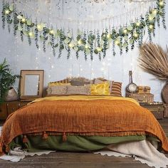 a bedroom decorated with greenery and string lights on the wall above the bed, along with an orange bedspread