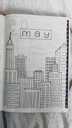 an open notebook with the word may written on it and cityscape in black ink