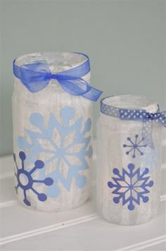 two jars decorated with snowflakes and blue ribbon on top of a white shelf