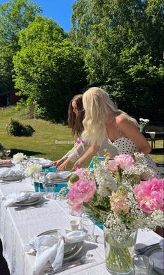 two women sitting at a table with plates and flowers in vases on the table