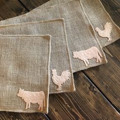 three placemats with farm animals on them sitting on a wooden table, one is made out of burlap