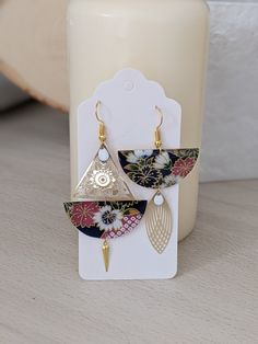 a pair of earrings sitting on top of a table next to a white container with a candle