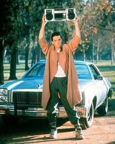 a man standing in front of a car holding up a pink book over his head