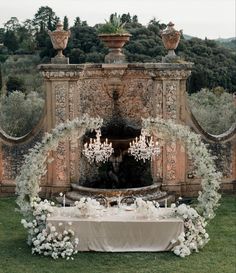 an outdoor wedding setup with chandeliers and flowers on the table, surrounded by greenery