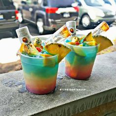 two cups filled with ice cream and fruit on top of a cement ledge next to parked cars