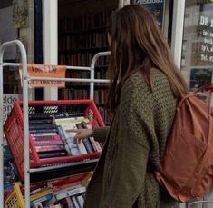 a woman with a backpack is looking at books in a book cart outside a bookstore