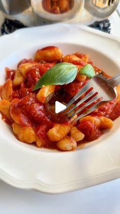 a white plate topped with pasta covered in sauce and garnished with green leaves