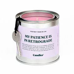 a pink candle in a metal tin with a black ribbon around the edge and a key hanging from it