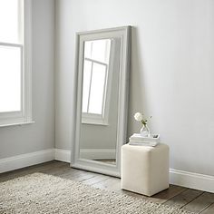 a mirror sitting on top of a wooden floor next to a white vase filled with flowers