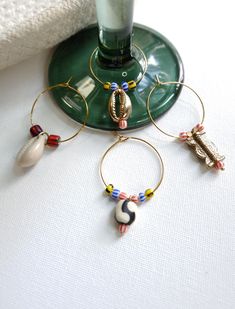 Add a unique touch to your wine glasses with this set of 4 handcrafted Wine Charms. Each charm is adorned with vibrant glass beads, brass accents, and a natural cowrie shell, creating a beautiful and functional accessory for your next gathering. Perfect for identifying your drink in style, these wine charms are a thoughtful addition to any occasion. Key Features: Handcrafted Design: Each charm is thoughtfully crafted with colorful glass beads, giving each piece a unique look. Brass Charms: Brass accents add a touch of elegance and sophistication to the design. Natural Cowrie Shells: Authentic cowrie shells provide another African-inspired element, making these charms perfect for any wine lover. Set of Four: Includes four distinct charms, so you and your guests can easily keep track of your Homemade Wine Charms, Beaded Wine Charms, Wine Glass Tags, Wine Glass Charm, Homemade Wine, Cowrie Shells, Wine Glass Charms, Brass Charms, Wine Charms