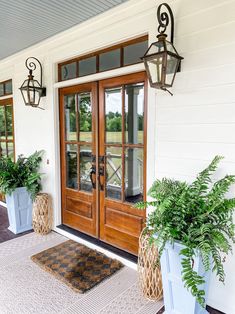 two planters are on the front porch of a white house with wood doors and windows