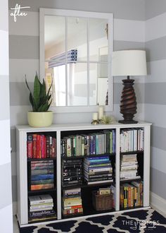 a bookshelf filled with lots of books next to a large mirror and lamp