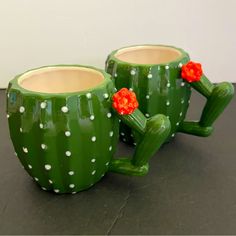 two green cactus mugs with red flowers on them sitting on a black counter top