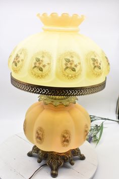 a yellow glass lamp sitting on top of a white table next to a flower vase