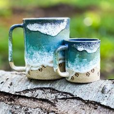 two coffee mugs sitting on top of a log