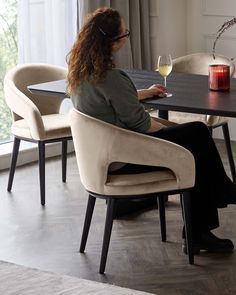 a woman sitting at a table with a glass of wine in her hand and looking out the window