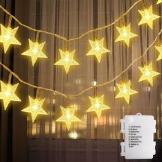 a string of yellow stars hanging from a curtain next to a window with curtains behind it