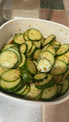 a white bowl filled with sliced cucumbers on top of a tiled countertop