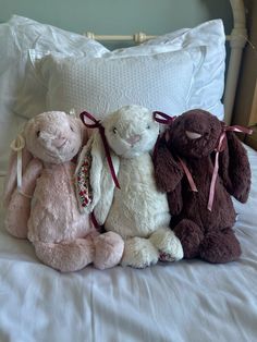 three stuffed animals sitting on top of a bed next to each other in front of a pillow