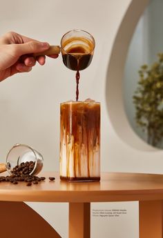 a person pouring coffee into a glass on top of a table