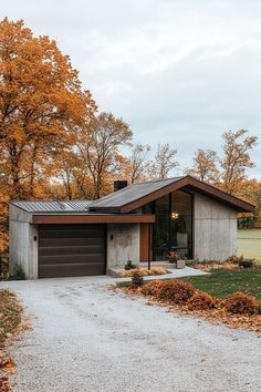 a modern house in the fall with orange leaves on the ground and trees around it