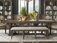 a dining room table with chairs and a bench in front of the table is an ornate china cabinet