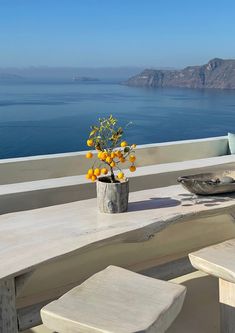 an outdoor table with flowers on it overlooking the ocean and mountains in the back ground