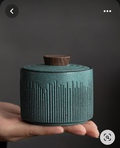 a hand holding a green ceramic container with a wooden cap on it's top