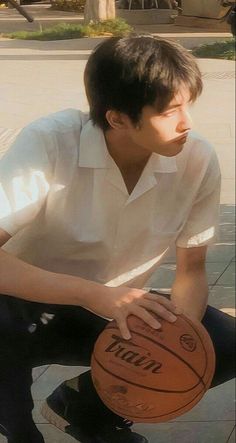 a young man is holding a basketball on the street while wearing black pants and a white shirt