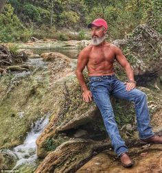 a man sitting on top of a rock next to a river in the woods with trees